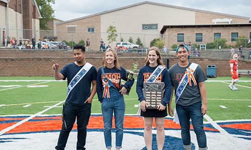 Carroll students standing on top of a football field with collegiate awards.